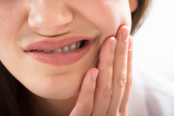 Young woman holds her jaw in pain before she sees Dr. Timothy H. Kindt, family dentist in Mesa AZ for gum disease treatment